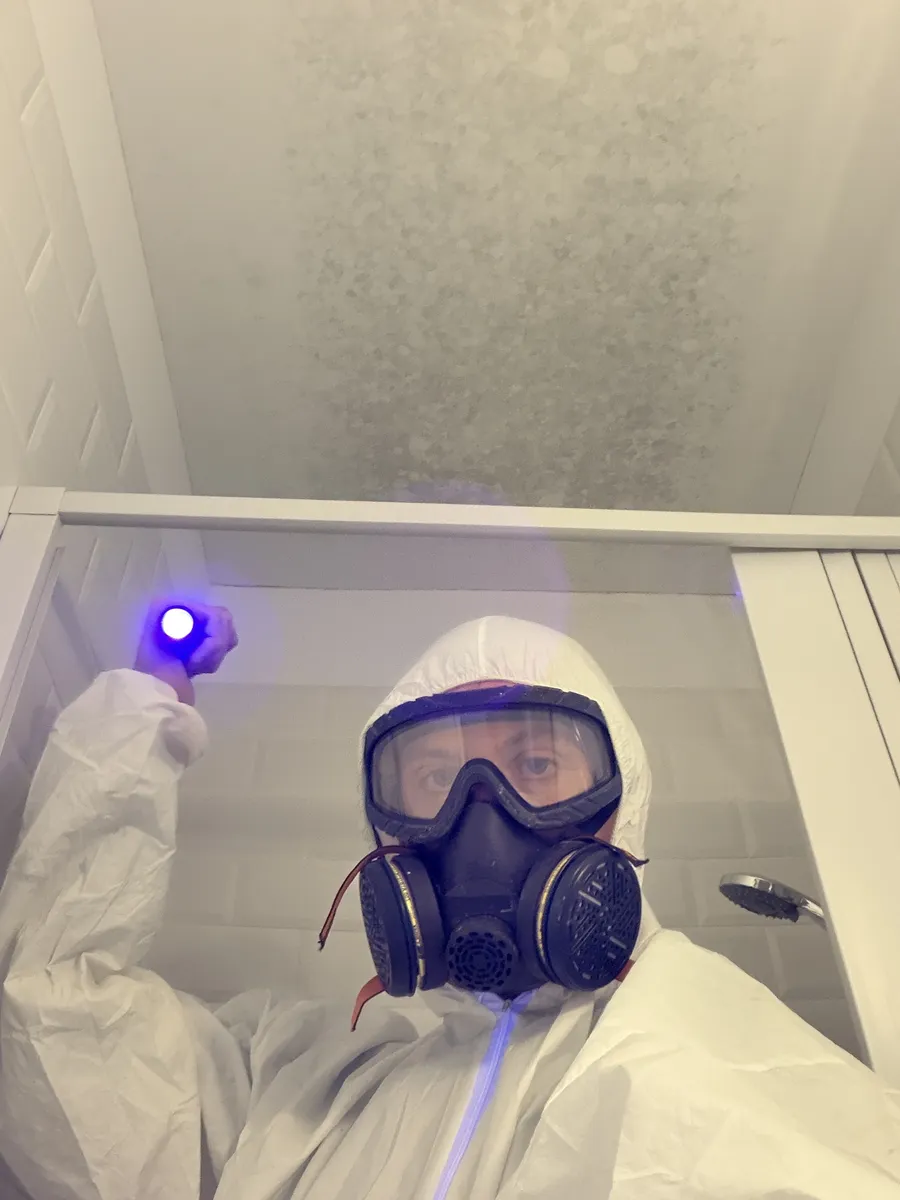 Especialista de Limpieza BCN con equipo de protección EPI y luz UV inspeccionando moho en techo de baño