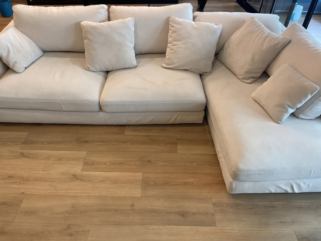 Sofá modular de diseño en tonos claros oscurecido por el polvo, mostrando ligeras marcas de agua y taninos antes de la limpieza profesional