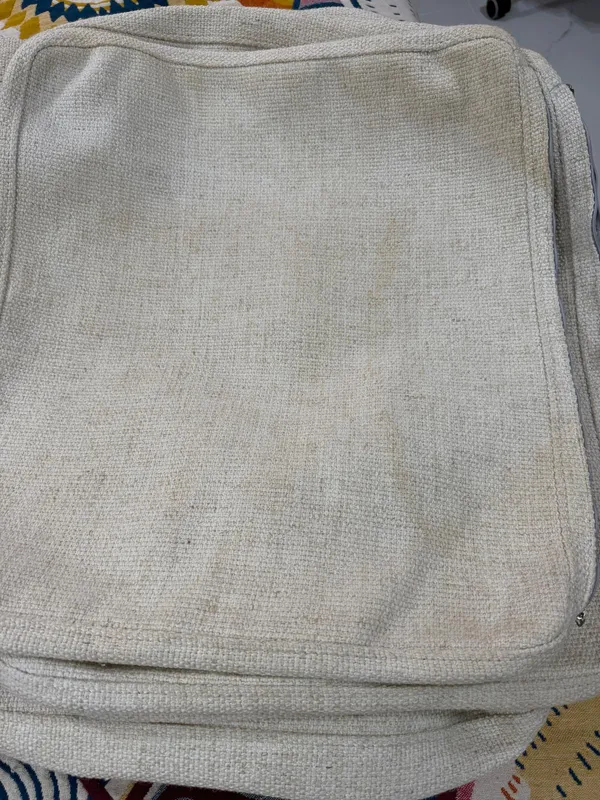Fundas desmontables de un sofá de algodón blanco con manchas de suciedad antes de la limpieza profesional