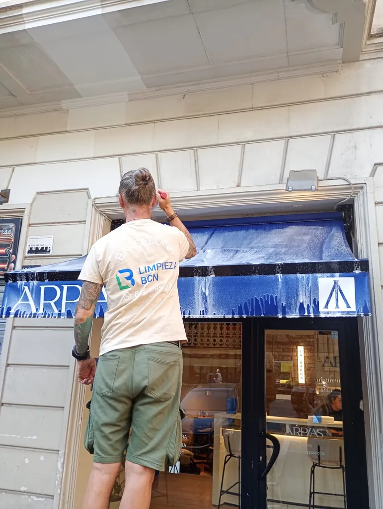 Operario de Limpieza BCN realizando la limpieza técnica de un toldo comercial con el uniforme de la empresa