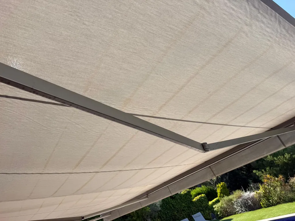 Efecto al trasluz de lona de toldo sucia | Limpieza BCN Toldo de lona con rayas negras y manchas de óxido visibles al trasluz desde el interior de la terraza