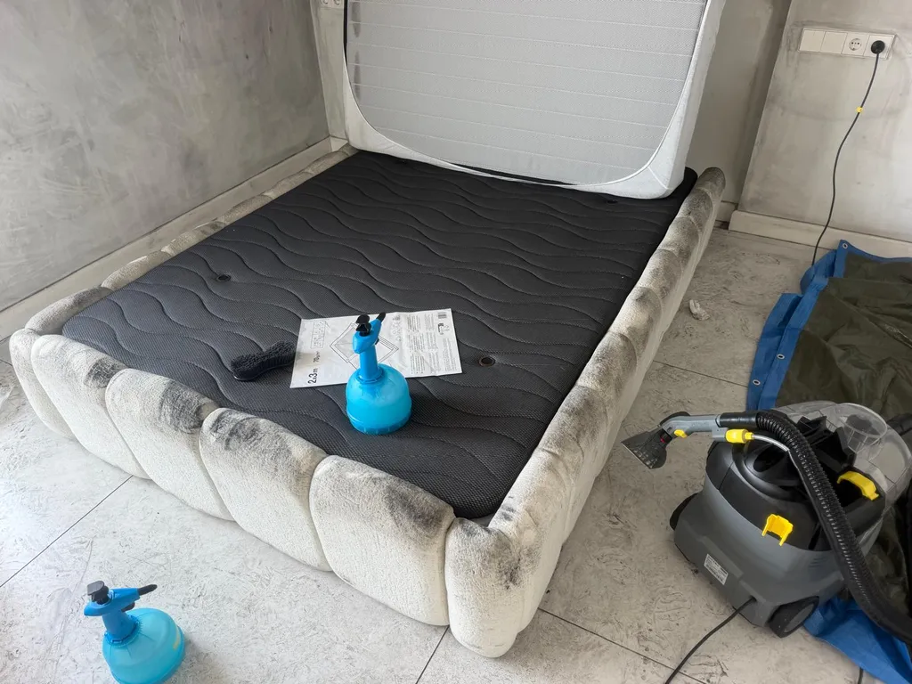Estructura textil de una cama desmontada con hollín severo junto a un aspirador de inyección-extracción profesional Kärcher Puzzi, lonas protectoras y pulverizadores en el suelo